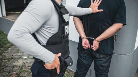Police officer making an arrest with force in Columbus, Ohio – suspect in handcuffs being restrained against a wall. Illustrates police use of force procedures.