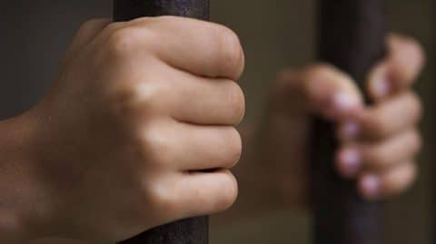 Hands Holding Onto the Bars of a Jail Cell