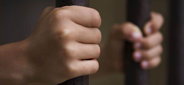 Hands Holding Onto the Bars of a Jail Cell