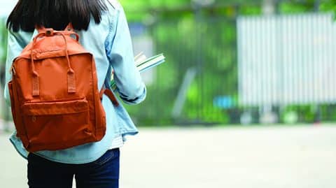 teenage girl holding books and wearing backpack