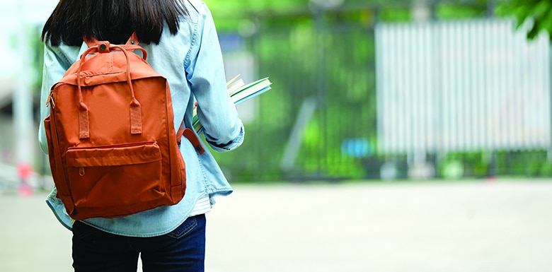 teenage girl holding books and wearing backpack